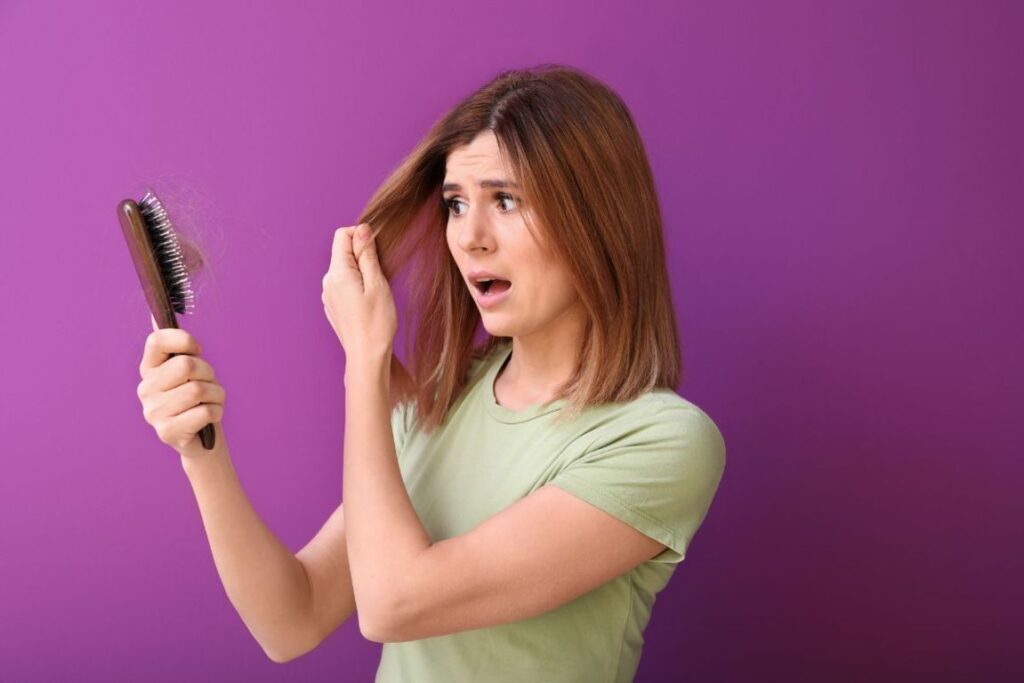 Donna con capelli castani osserva preoccupata una spazzola piena di ciocche cadute su sfondo viola