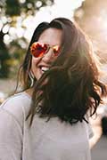 Donna che sorride con capelli mossi e occhiali da sole tra i capelli