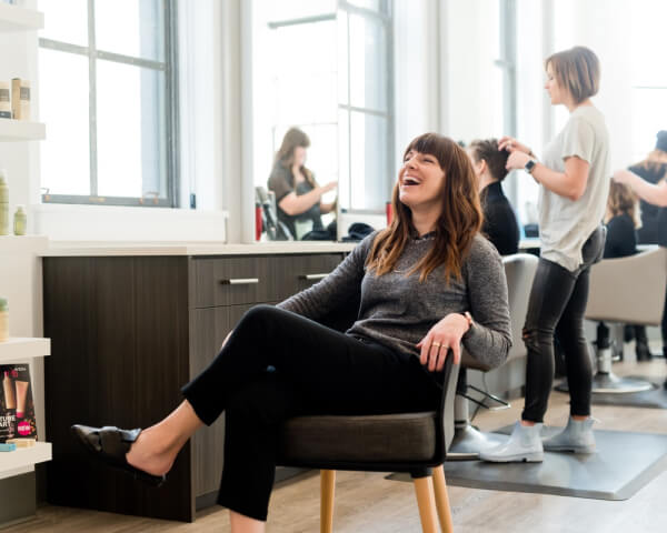 Cliente sorridente seduta nel salone Lucy Hairstyle, con parrucchiera al lavoro sullo sfondo